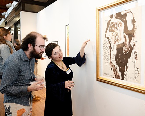 Patrons look at a piece at the exhibit, "Abstract Activism: Sam Maitin's Philadelphia."