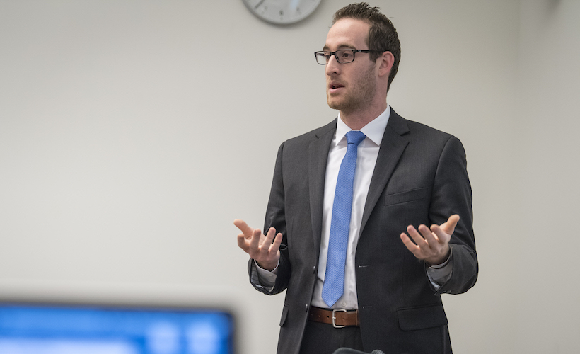 A student stands, gesturing with his hands, as he speaks.